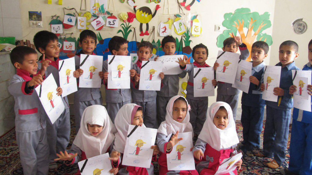 Children sing the firefighters anthem holding a picture of a firefighter book character with a black ribbon - Read with Me in South Khorasan - January 2017